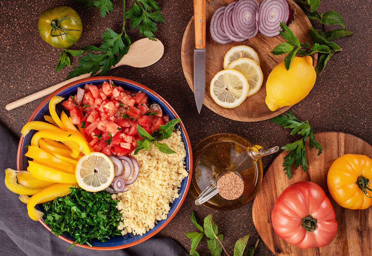 Plates featuring assortment of halal foods, tomatoes, peppers, onion, herbs, lemon and olive oil.