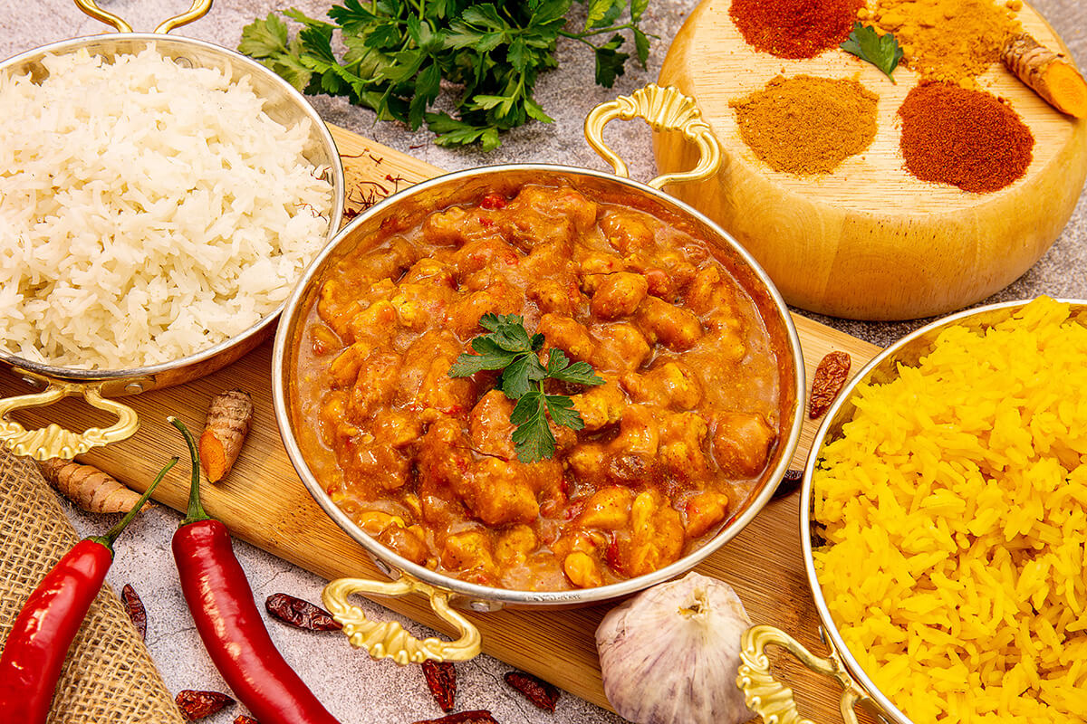 indian chicken curry, rice and spices served on wooden platter