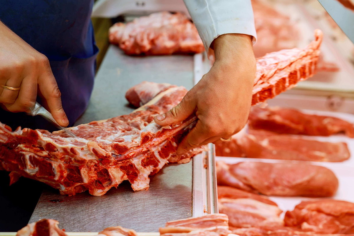 man butchering beef ribs behind meat department counter 