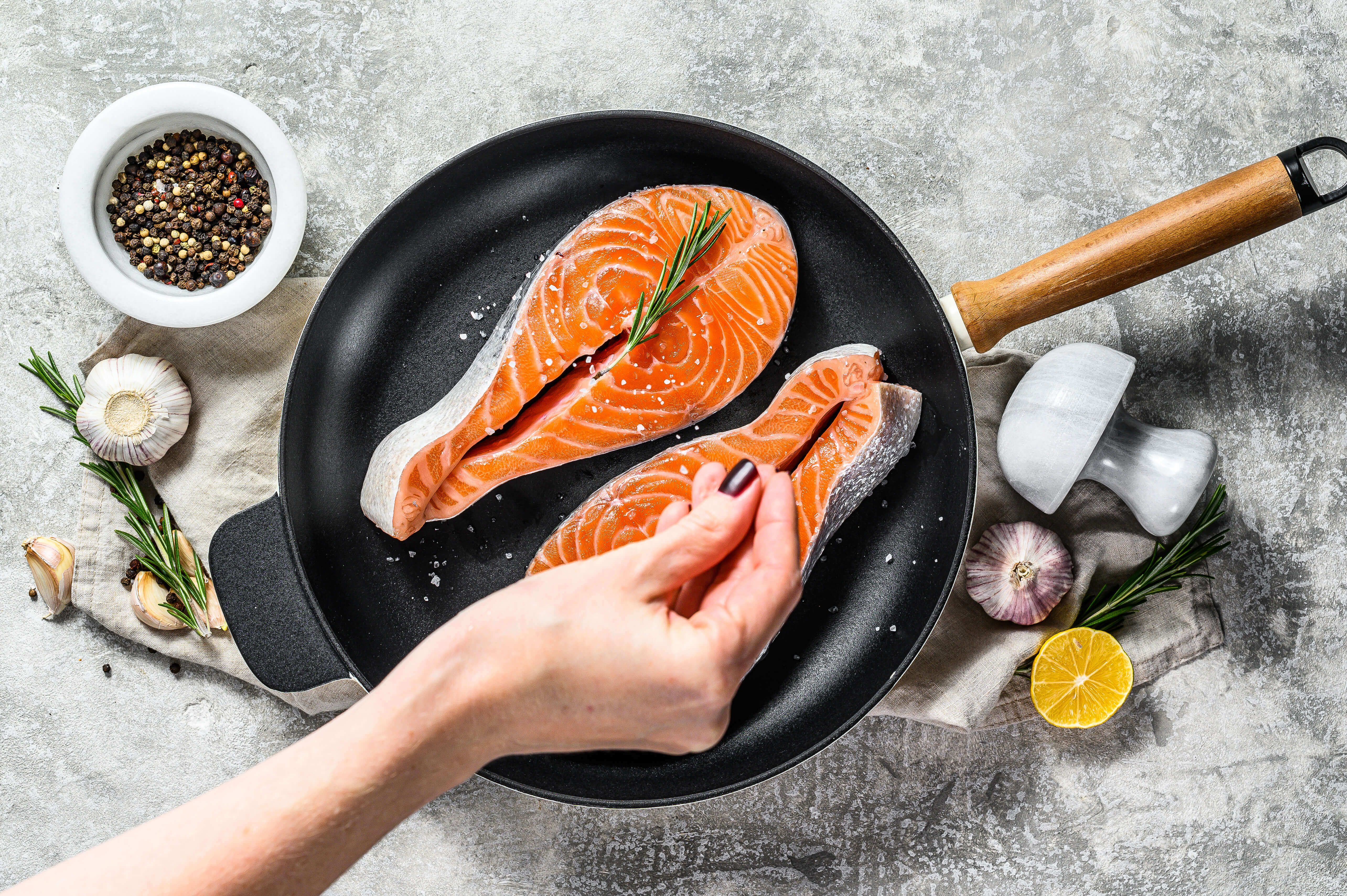 person putting salt on cuts of raw salmon in a pan